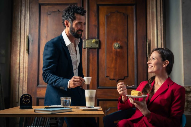 Eine Frau und Mann lächeln sich an und genießen währendessen Kaffee und Kuchen.