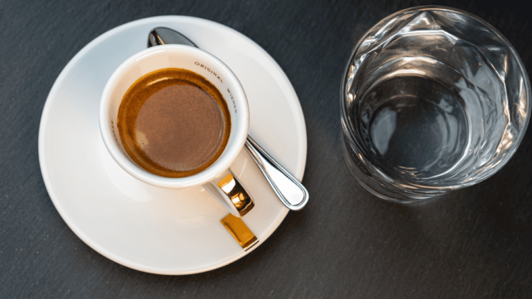 Eine Tasse Espresso in Bio-Qualität von fabia und ein Glas Wasser von oben fotografiert