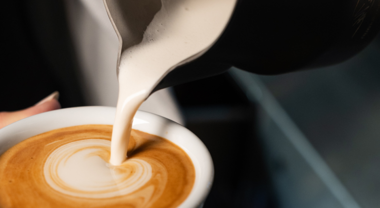 Milchkännchen schüttet den Milchschaum in eine Tasse